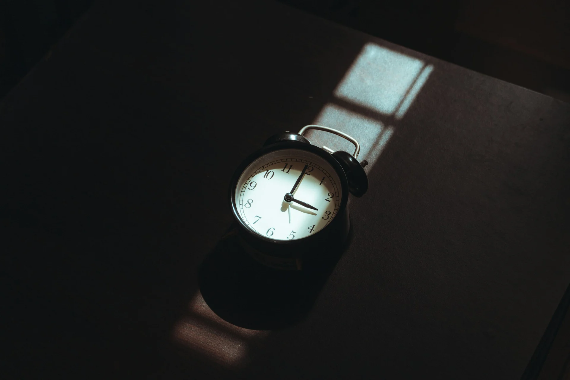 man reaching over to switch off an alarm clock in a dark bedroom before sunrise