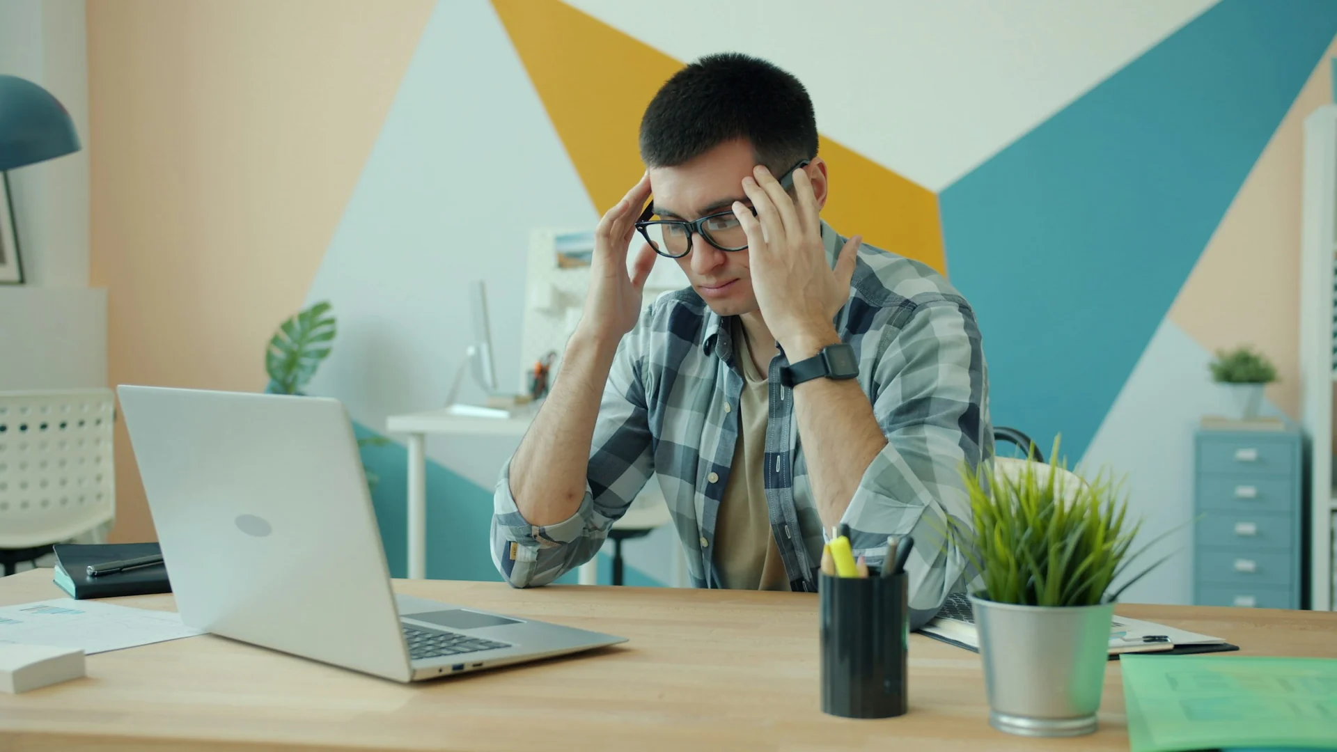 tired man rubbing his eyes at a desk in an open-plan office in the afternoon