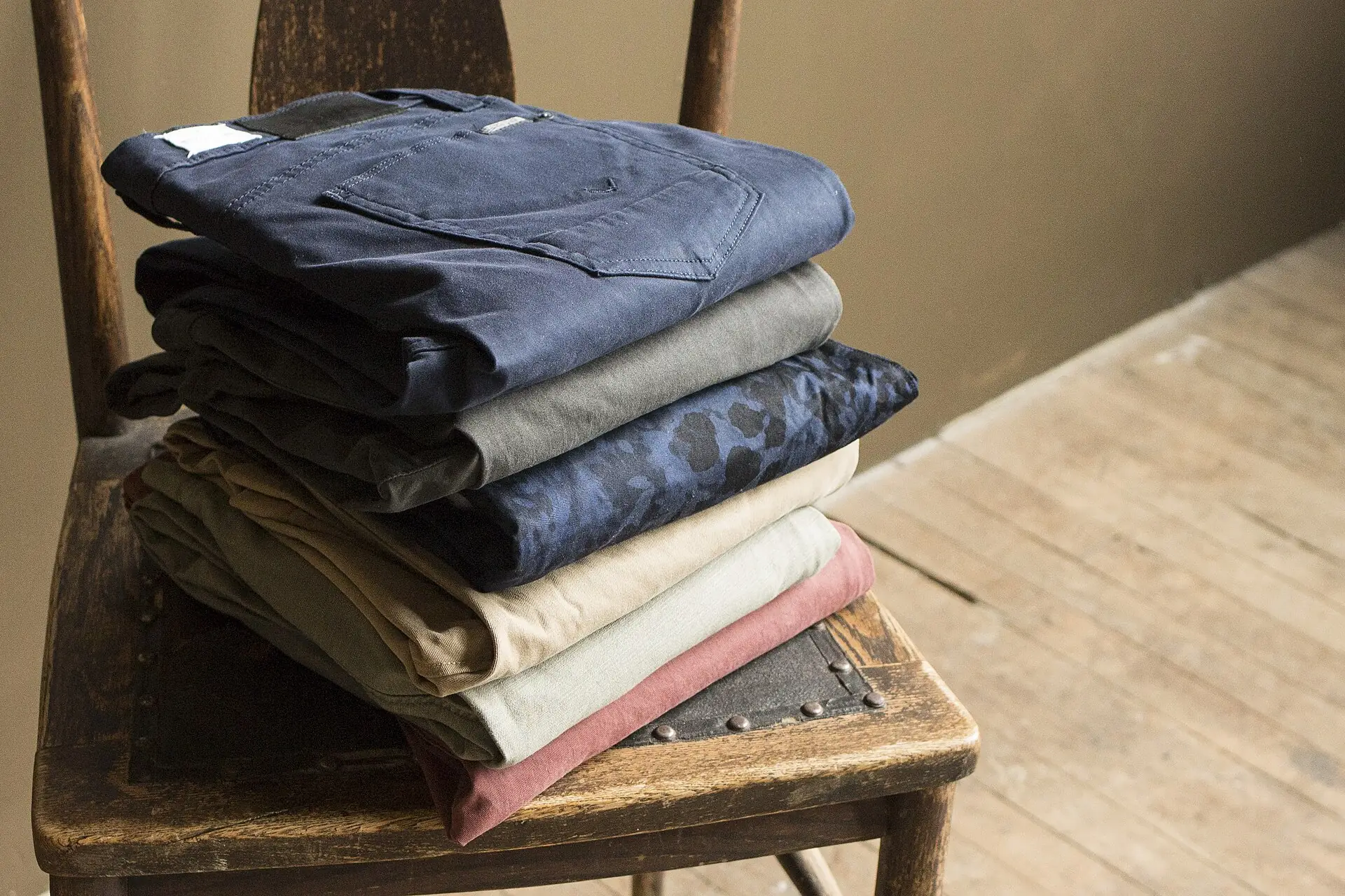 folded pair of khaki chinos next to folded indigo jeans on a bed